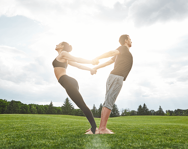 Man and woman performing a partnered yoga pose outdoors at sunset.